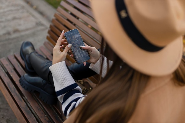 Attractive cheerful brunette girl in trench coat with coffee to go happily using cellphone outdoor