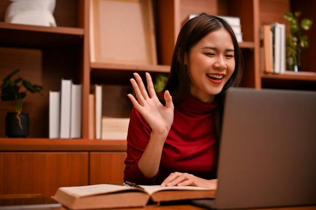 Attractive and cheerful young Asian businesswoman greeting her online meeting