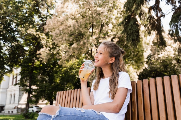 Attractive child girl drinking summer lemonade Summer cocktails Happy girl holding cup with orange lemonade outdoor