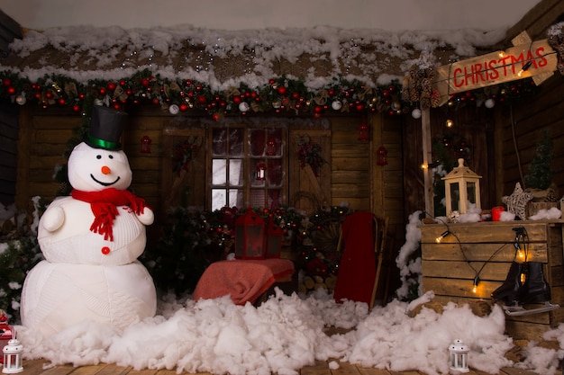 Attractive Christmas Decoration Inside a Wooden House with Large Winter Snowman, Cotton Snow on the Floor and Lighted Wooden Christmas Booth.