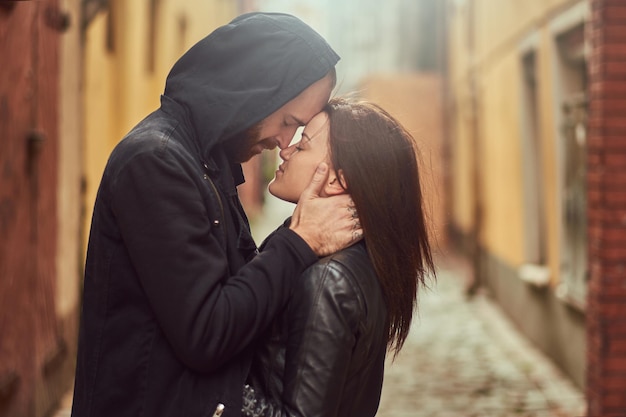 Attractive couple, bearded man and brunette girl kissing outside old European street on a background.