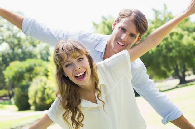 Attractive couple smiling at camera and spreading arms in the park