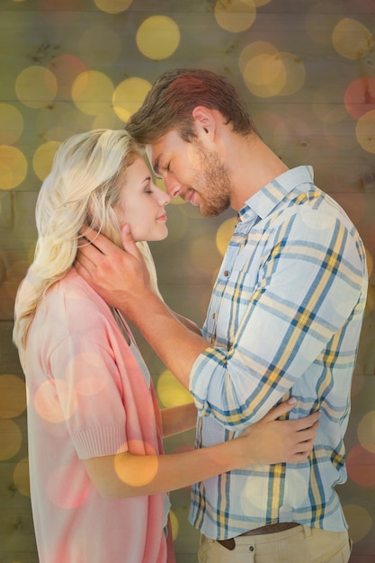 Attractive couple smiling at each other and hugging against close up of christmas lights