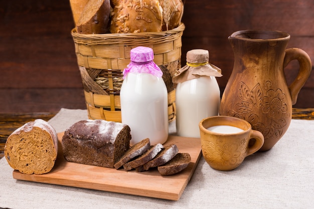 Attractive display of rustic breads in a woven basket a jug and cup of milk and a half sliced loaf of pumpernickel on a cutting board