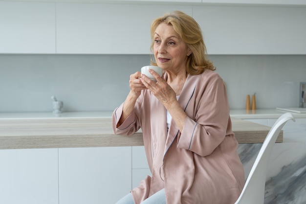 Attractive elderly woman enjoying a cup of coffee in her kitchen thinking in appreciation