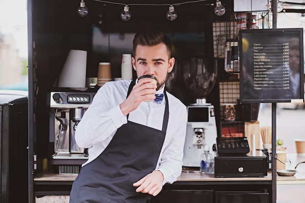 Attractive elegant barista is drinking coffee while waiting for customers at his own small coffeeshop.