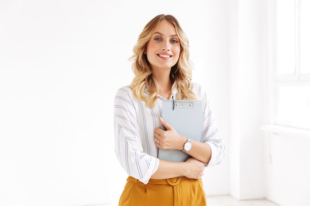 attractive elegant businesswoman smiling and holding clipboard in white office