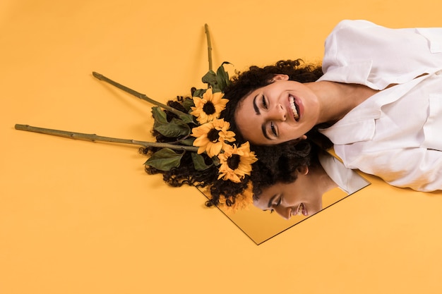 Attractive ethnic smiling woman with flowers on mirror