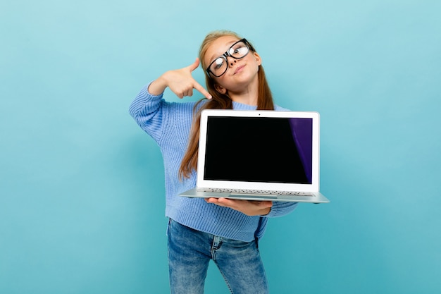 Attractive european girl shows a laptop screen with mockup in her hands on light blue