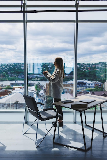 Attractive female blogger in a jacket with a modern smartphone in her hands thoughtful and daydreaming a young blogger holding a mobile phone reflects on social media posts