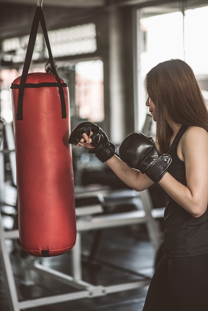 Attractive female boxer training with kick boxing at gym with blackgloves.