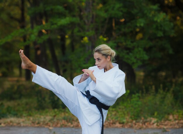 Attractive female master fighter in white kimono with black belt kicks outdoors
Â 
