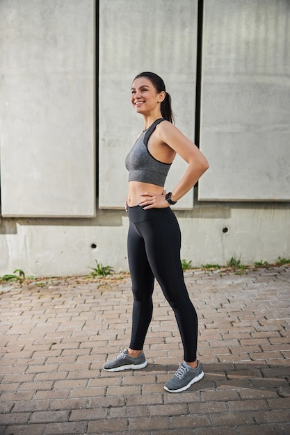 Attractive female person keeping smile on her face while standing on the sidewalk and waiting for her partner