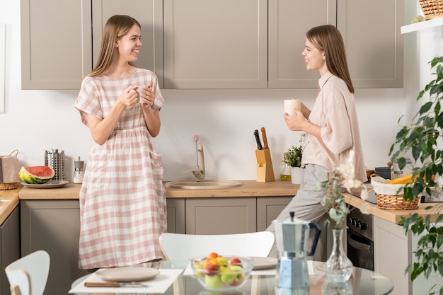 Attractive female teenage twins with drinks interacting in the kitchen