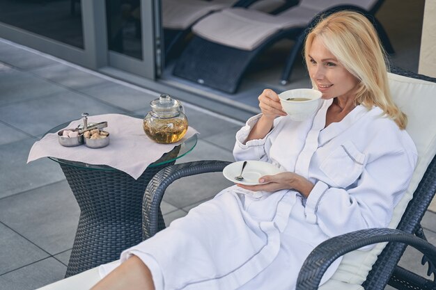 attractive female in white soft bathrobe while drinking tea in the morning