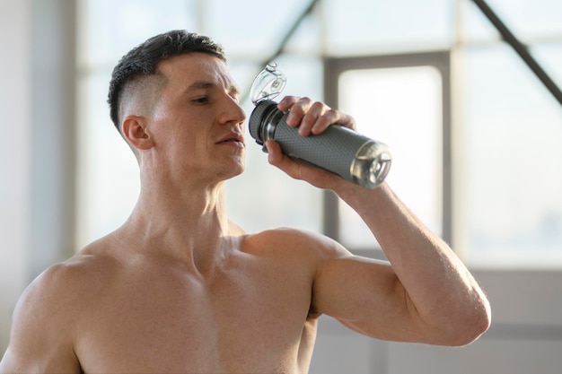 Attractive fit man drinking water after training indoors Healthy lifestyle training in gym