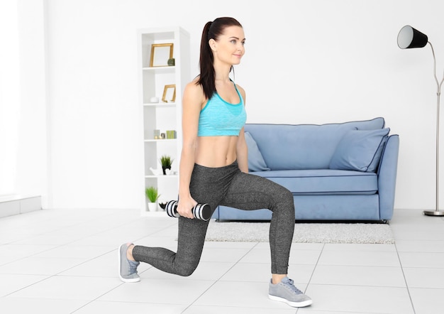 Attractive fitness woman exercising with dumbbells at home