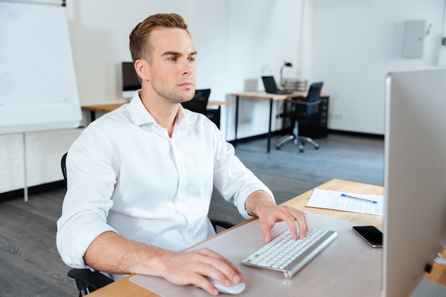 Attractive focused young businessman sitting in office and using computer