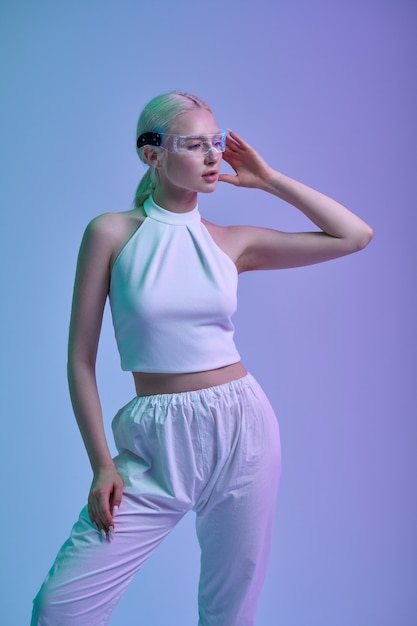 Attractive futuristic woman in white clothes and modern glasses, grey background. Sexy female person in virtual reality style, future technology, futurism concept