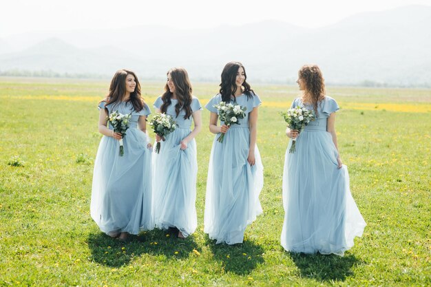 attractive gentle bridesmaids standing in nice dresses and with bouquets in hands and having fun