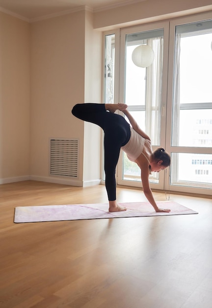 Attractive ginger girl practicing yoga in Reclined Spinal Twist pose Woman stretching on pink mat in Supta Matsyendrasana yoga pose Fitness training at home or gym class Healthy lifestyle concept