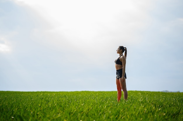 Attractive girl athlete does warm-up outdoors, exercises for muscles. Young woman go in for sports, healthy lifestyle, athletic body. She is in sportswear, black top and shorts