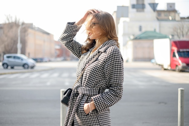 Attractive girl in a coat in the street in a city, sun is shining, than turns to camera and smiles. portrait happy slow motion summer face sunset beautiful lady outdoor closeup cute