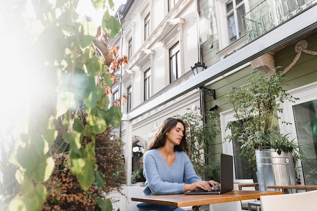 Attractive girl freelancer is working online on laptop in cafe outdoor Confident business woman manager with laptop is working with colleagues online in cafe