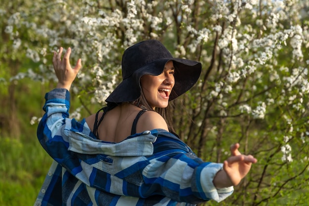 Attractive girl in a hat among the flowering trees in the spring, in a casual style.