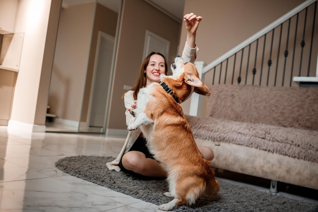 Attractive girl hug and play with corgi dog at home Welsh Corgi Pembroke with his owner woman on the floor at living room