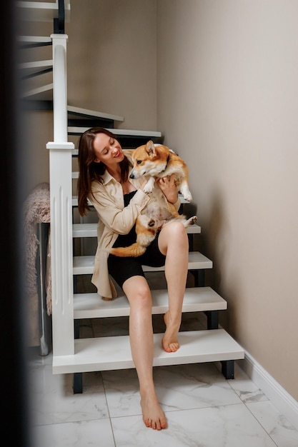 Attractive girl hug and play with corgi dog at home Welsh Corgi Pembroke with his owner woman sitting on the stairs