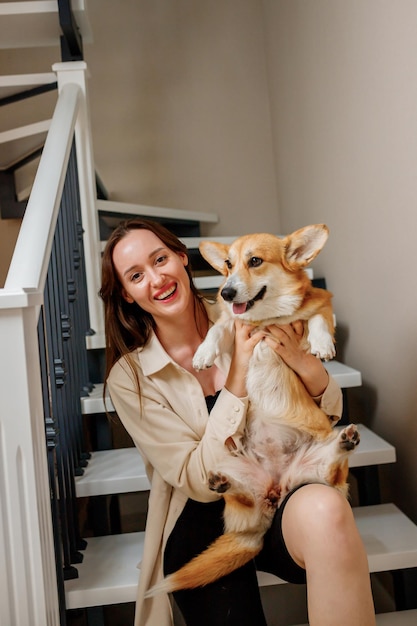 Attractive girl hug and play with corgi dog at home Welsh Corgi Pembroke with his owner woman sitting on the stairs