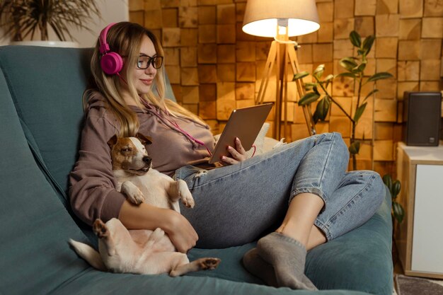 Photo attractive girl listens to music and watches video clips on a tablet as a dog in a home environment indoors