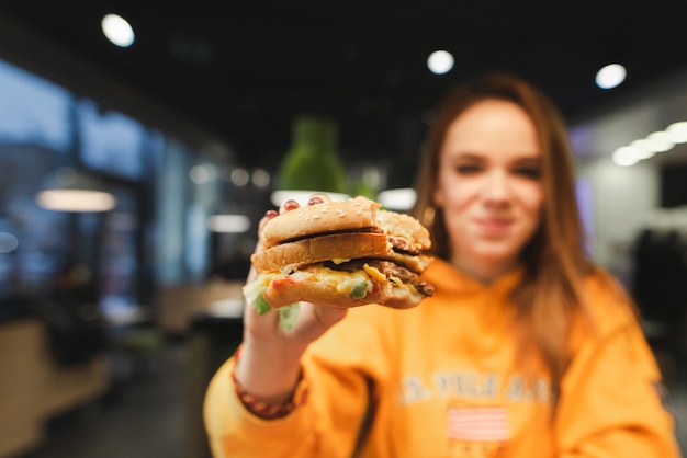 Attractive girl in orange clothes holding a big tasty burger