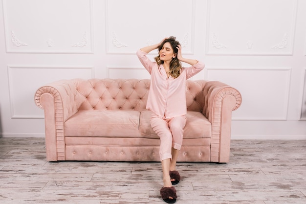 Attractive girl playing with hair on couch Indoor shot of winsome woman chilling on sofa