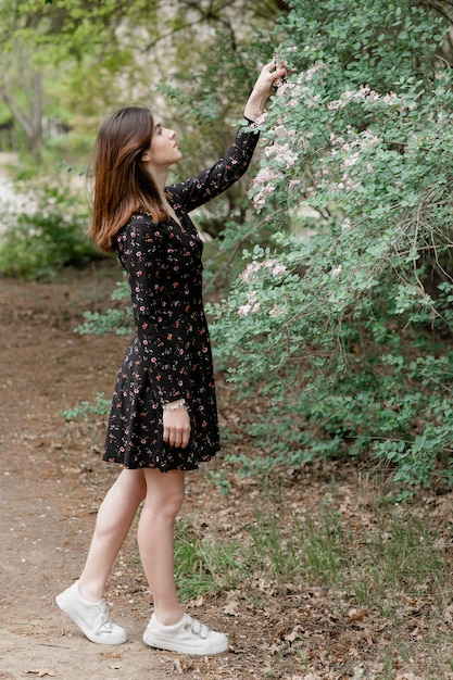 Attractive girl standing in blooming garden touching blossom looking up admiring