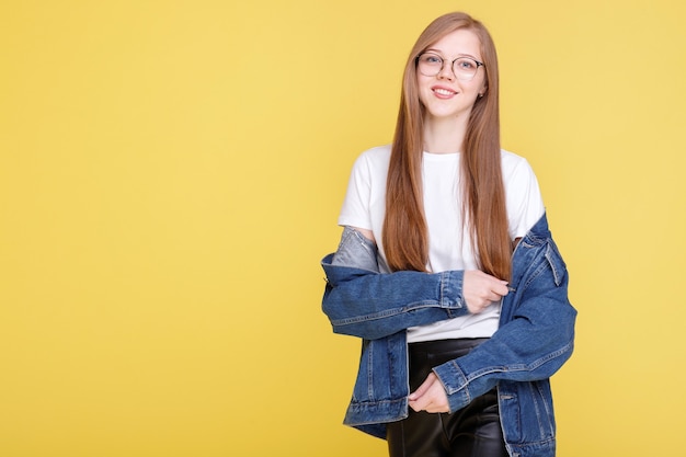 Attractive girl student in glasses smiles on a yellow wall