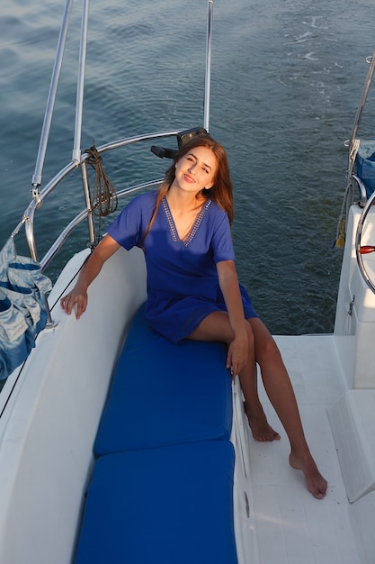 Attractive girl on a yacht at summer day. Close up of fashion portrait of stunning romantic woman posing yacht. Wearing an elegant dress, summer outfit. Blue sky. sunset