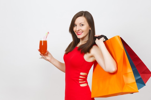 Attractive glamour fashionable young woman in red dress holding glass of drink cocktail, multi colored packets with purchases after shopping isolated on white background. Copy space for advertisement.