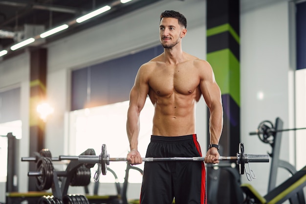 Attractive guy doing biceps exercises with barbell at the modern gym. Sporty and healthy concept.