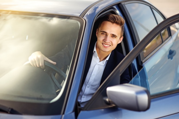 Attractive handsome smiling man in a business suit driving an expensive car