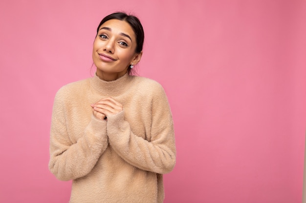 Attractive happy cute nice adorable tender young brunette woman in casual beige sweater isolated on pink background with free space and enjoying