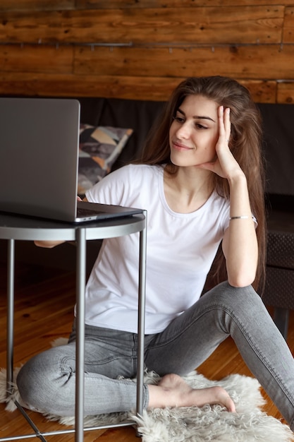 Attractive happy smiling girl student having video chat sitting on the floor