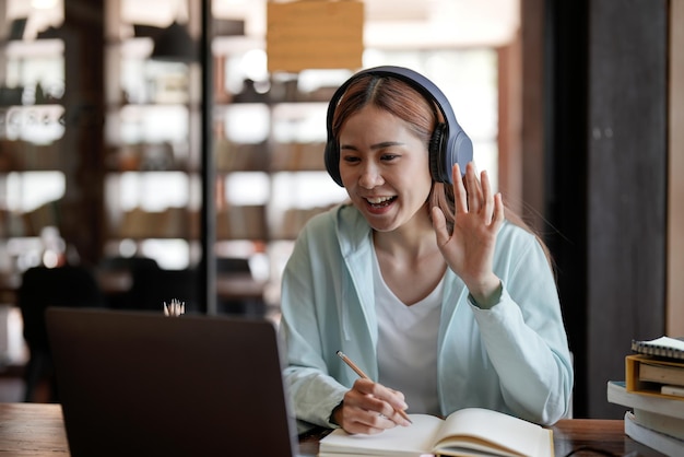 Attractive happy young student studying online at home using laptop computer headphones having video chat waving Remote work distance education Video conference or virtual event on quarantine