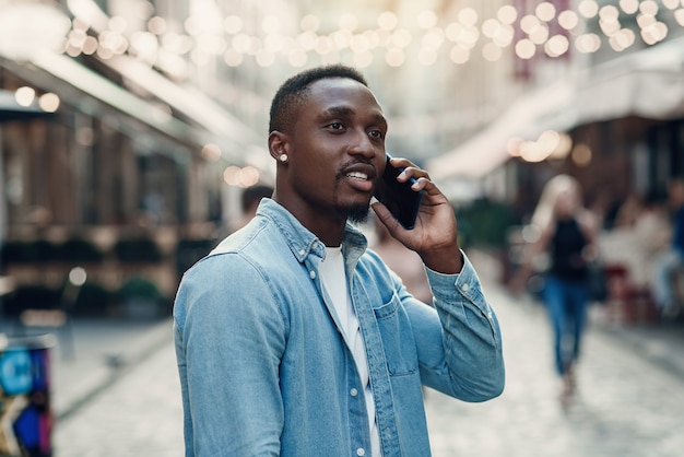 Attractive joyful afroamerican guy with stylish beard has phone conversation during walking on the