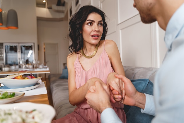 Attractive lady looking at boyfriend with amazed expression while man holding her hands