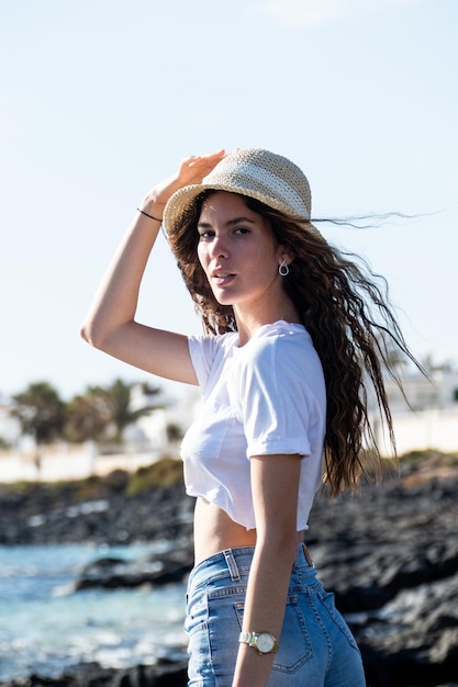 Attractive latin young woman portrait outdoors by the sea wearing a hat and summer clothes