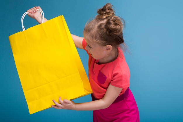 Attractive little cute girl in pink dress holds yellow paper bag