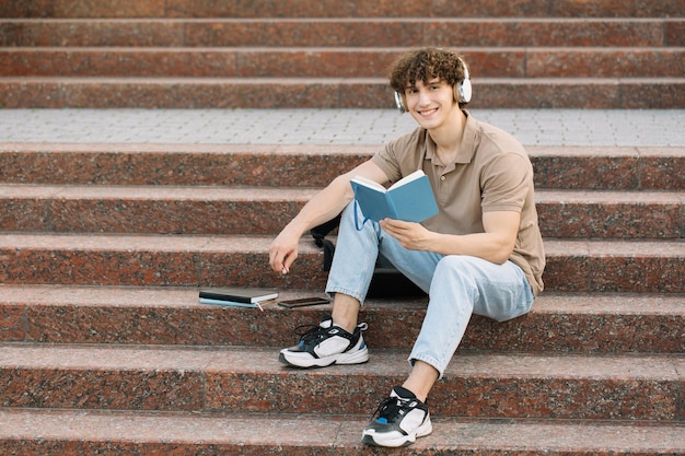 Attractive male student sits on the steps of the university and reads something preparing for exams