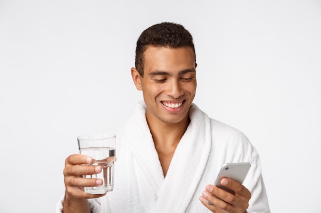 An attractive man drinking a glass of water against white